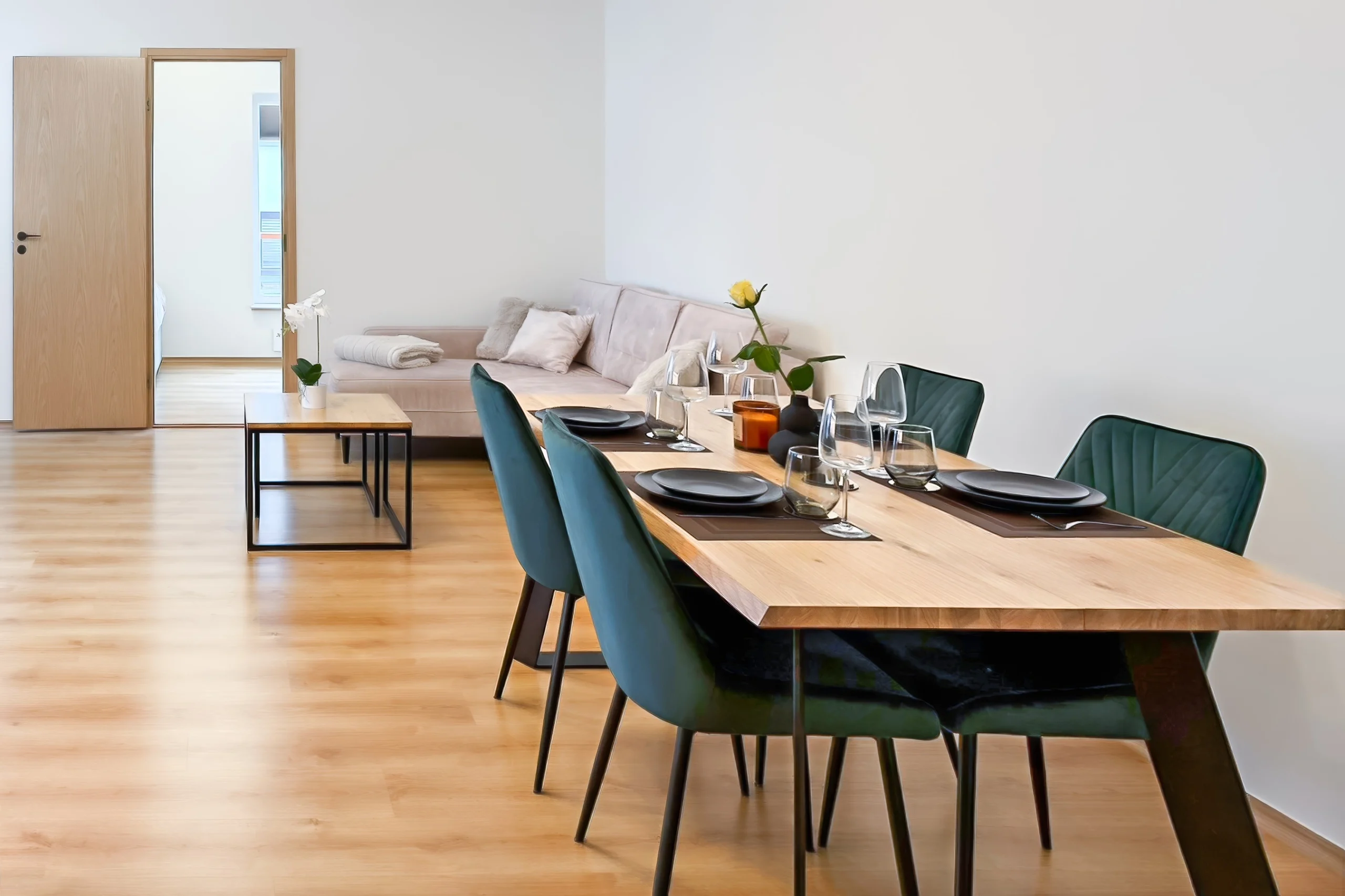 Kuressaare Stays korteri sisekujundus: Söögilaud roheliste velvettoolidega ja elutuba mugava diivaniga avatud planeeringuga korteris.